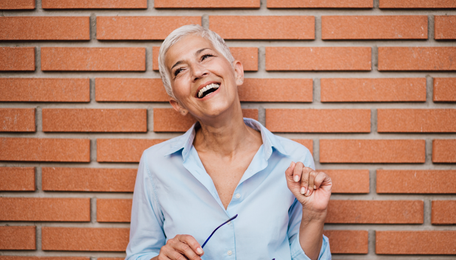 a woman looking happy in a business shirt against a brick wall.